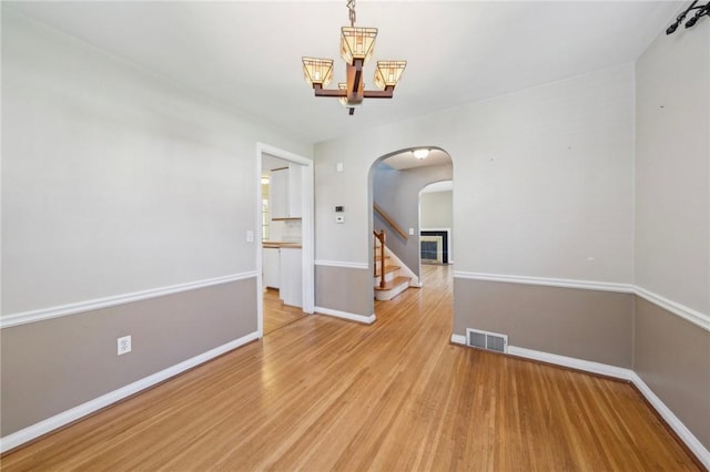 spare room featuring visible vents, wood finished floors, baseboards, arched walkways, and a notable chandelier