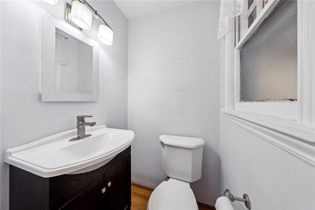 half bathroom with vanity, wood finished floors, and toilet