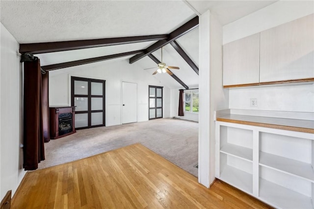 unfurnished living room with carpet floors, ceiling fan, vaulted ceiling with beams, and wood finished floors