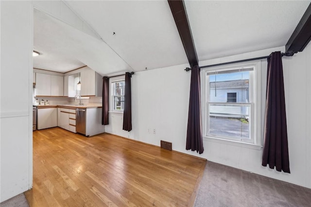 unfurnished living room with visible vents, a sink, lofted ceiling with beams, and light wood-type flooring