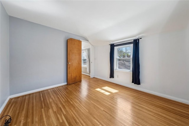 unfurnished room with light wood-type flooring, baseboards, and vaulted ceiling
