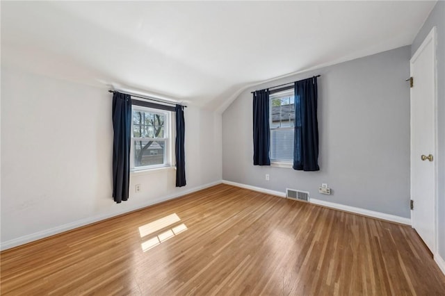 spare room with visible vents, a healthy amount of sunlight, lofted ceiling, and wood finished floors
