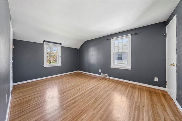 additional living space with baseboards, lofted ceiling, wood finished floors, and visible vents
