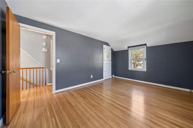 empty room with baseboards, light wood finished floors, and vaulted ceiling