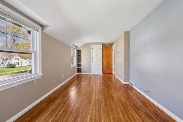 empty room featuring visible vents, built in features, wood finished floors, baseboards, and lofted ceiling