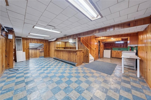 finished below grade area featuring wooden walls, bar, washer / dryer, and tile patterned floors
