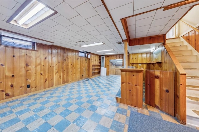 below grade area featuring wooden walls, a dry bar, tile patterned floors, visible vents, and stairway