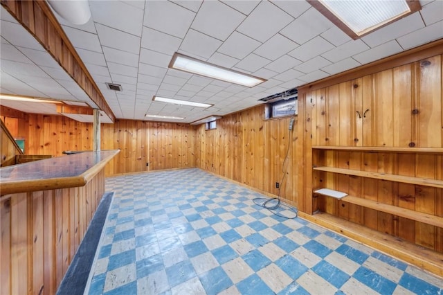 below grade area featuring tile patterned floors, wood walls, a dry bar, and visible vents