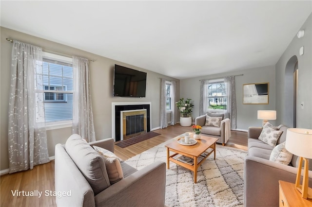 living room featuring a fireplace with flush hearth, arched walkways, baseboards, and wood finished floors