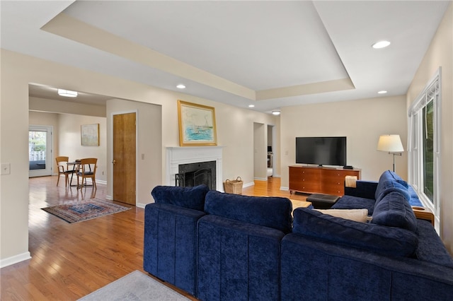 living area with recessed lighting, a tray ceiling, wood finished floors, and a fireplace