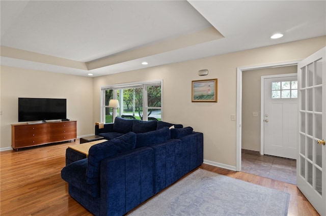 living room with baseboards, a tray ceiling, a healthy amount of sunlight, and light wood-style floors
