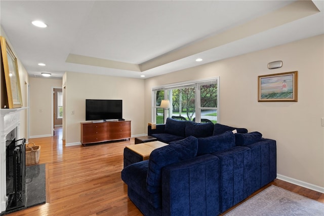living room featuring light wood-style floors, recessed lighting, baseboards, a high end fireplace, and a tray ceiling