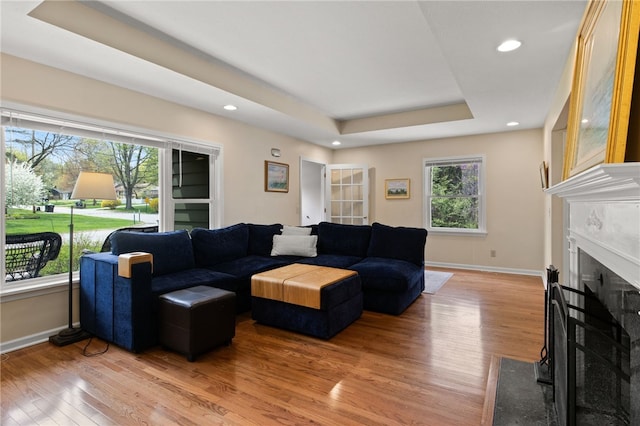 living room with baseboards, recessed lighting, a raised ceiling, a fireplace with flush hearth, and light wood finished floors