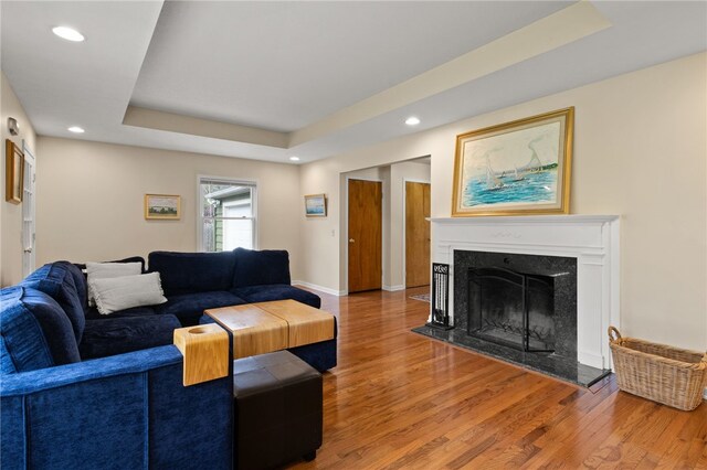 living area with wood finished floors, baseboards, recessed lighting, a high end fireplace, and a raised ceiling
