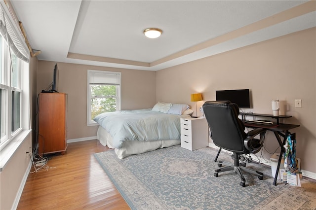 bedroom with baseboards, a tray ceiling, and light wood-style floors