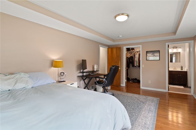 bedroom with a closet, light wood-style floors, baseboards, a walk in closet, and a raised ceiling