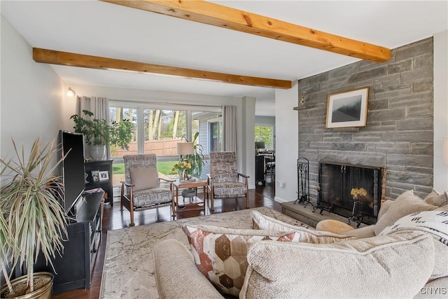 living area featuring a healthy amount of sunlight, beamed ceiling, a stone fireplace, and wood finished floors