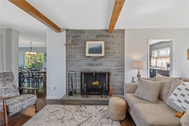 living area with beam ceiling, a stone fireplace, and wood finished floors
