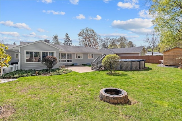 rear view of property featuring a fenced in pool, a fire pit, fence, and a shed