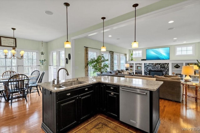 kitchen with a sink, dark cabinetry, a premium fireplace, a healthy amount of sunlight, and stainless steel dishwasher