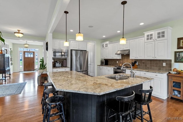 kitchen featuring appliances with stainless steel finishes, a sink, a kitchen breakfast bar, wood finished floors, and under cabinet range hood