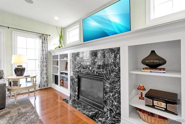 living area with built in shelves, a fireplace, and wood finished floors