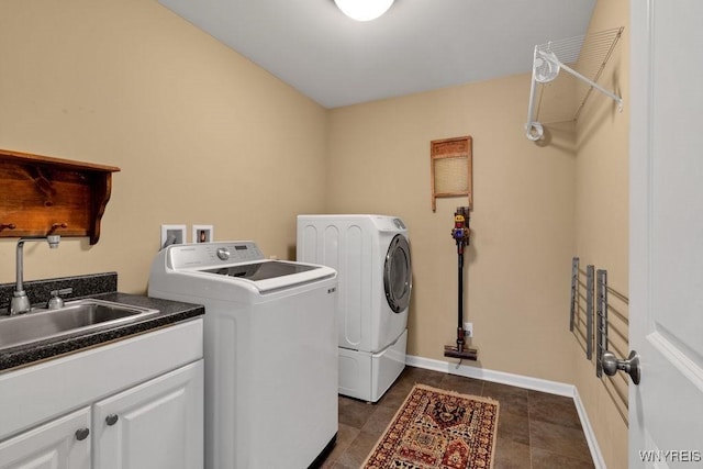 clothes washing area with cabinet space, a sink, separate washer and dryer, baseboards, and dark tile patterned floors