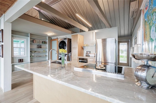 kitchen featuring freestanding refrigerator, stacked washer / dryer, black electric cooktop, light stone counters, and a sink