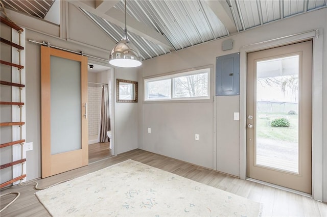 interior space with vaulted ceiling with beams, electric panel, light wood finished floors, and a barn door