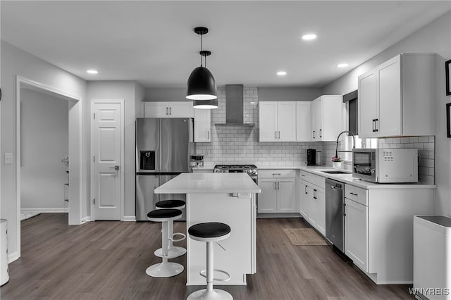 kitchen with a sink, wall chimney exhaust hood, stainless steel appliances, white cabinetry, and a kitchen island