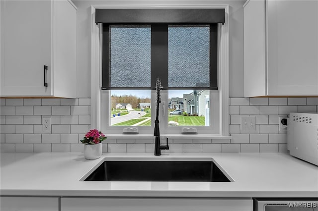 kitchen with a sink, light countertops, white cabinets, and tasteful backsplash