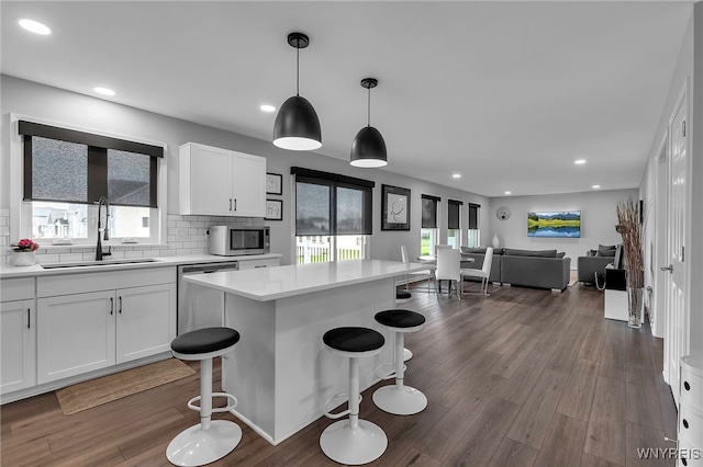 kitchen featuring a kitchen breakfast bar, a sink, light countertops, white cabinets, and open floor plan