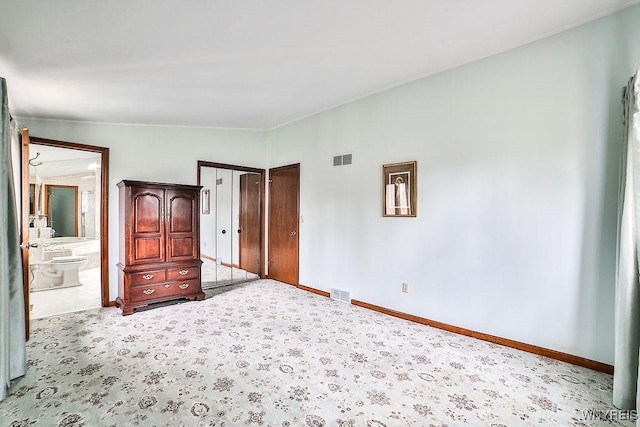unfurnished bedroom with baseboards, ensuite bathroom, carpet flooring, and visible vents