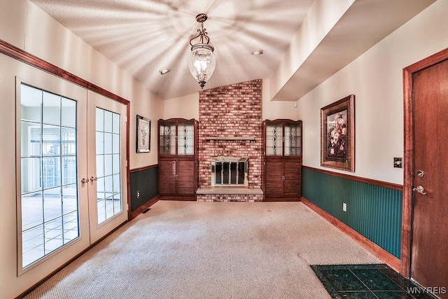 unfurnished living room featuring french doors, a fireplace, a wainscoted wall, carpet floors, and lofted ceiling