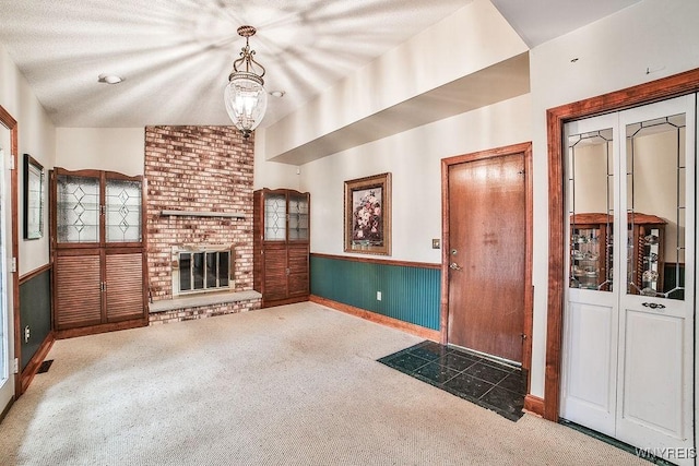 unfurnished living room featuring a fireplace, baseboards, a wainscoted wall, carpet, and vaulted ceiling