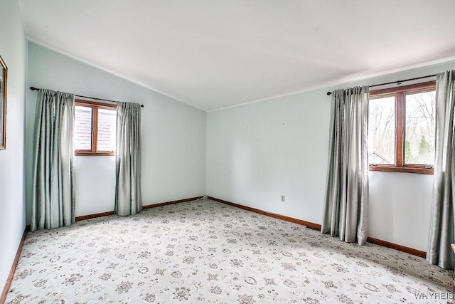 empty room featuring carpet flooring, baseboards, and vaulted ceiling