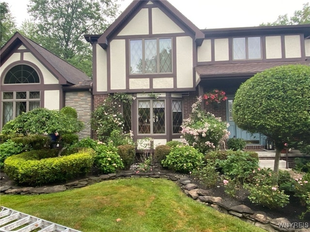 back of house with brick siding, a shingled roof, stucco siding, and a yard