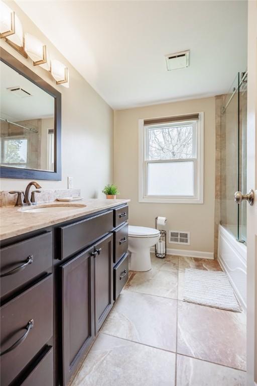 bathroom with vanity, toilet, shower / bath combination with glass door, and visible vents