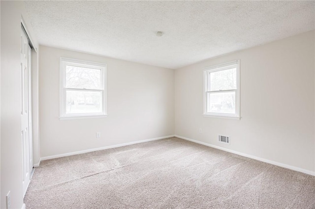 carpeted spare room featuring baseboards, a textured ceiling, and visible vents
