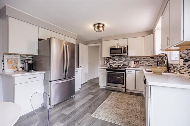 kitchen featuring light countertops, a sink, light wood-style flooring, backsplash, and stainless steel appliances
