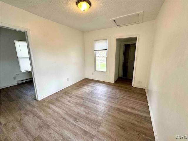 unfurnished room featuring baseboards, a baseboard radiator, a textured ceiling, and attic access