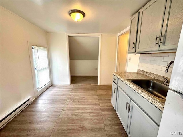 kitchen with light wood-style floors, baseboard heating, light countertops, tasteful backsplash, and a sink