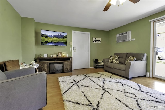 living area featuring wood finished floors, baseboards, ceiling fan, and a wall unit AC
