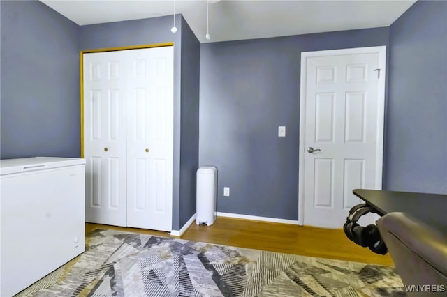 bedroom with baseboards, a closet, fridge, and wood finished floors