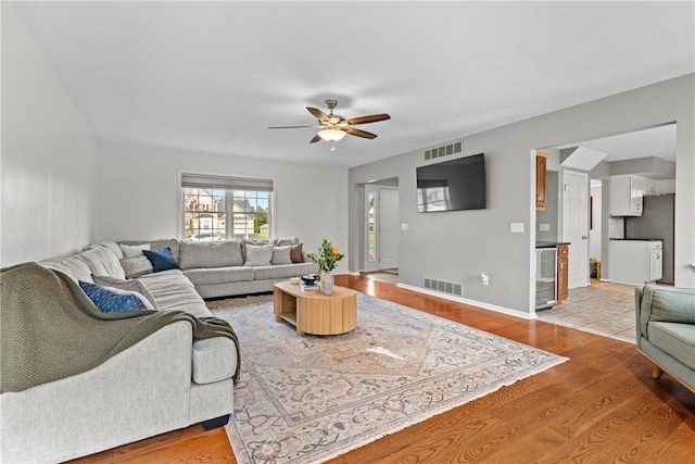 living room with a ceiling fan, visible vents, beverage cooler, and light wood-type flooring
