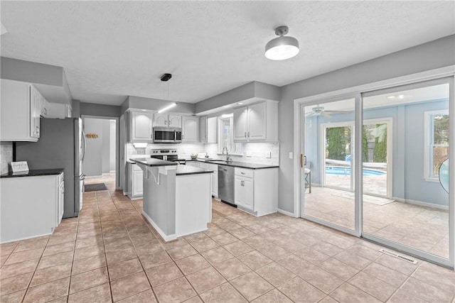 kitchen with light tile patterned flooring, dark countertops, appliances with stainless steel finishes, a sink, and a center island
