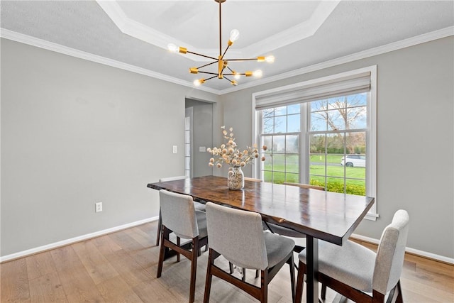 dining room with an inviting chandelier, ornamental molding, baseboards, a raised ceiling, and light wood finished floors