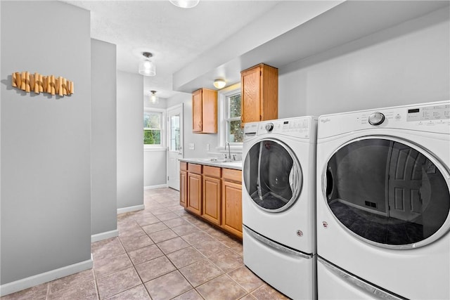 clothes washing area with cabinet space, a sink, baseboards, light tile patterned floors, and washer and dryer