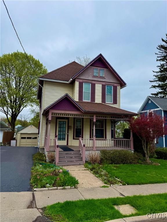 victorian-style house featuring covered porch, an outdoor structure, and a garage
