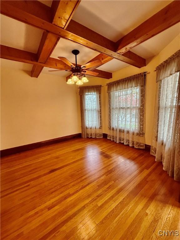 empty room with baseboards, a ceiling fan, wood finished floors, and beamed ceiling